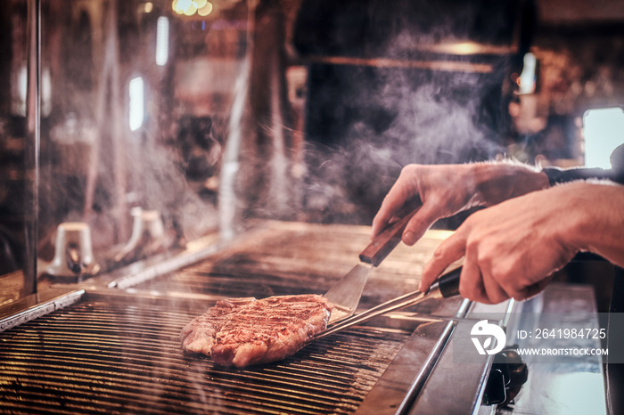 Close-up image of a cooking delicious meat steak on a grill in a restaurant kitchen.