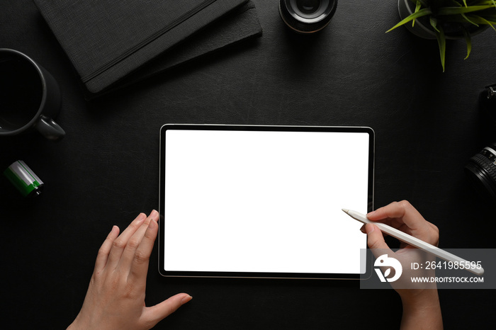 Top view of female hands using digital tablet with stylus pen on dark workspace