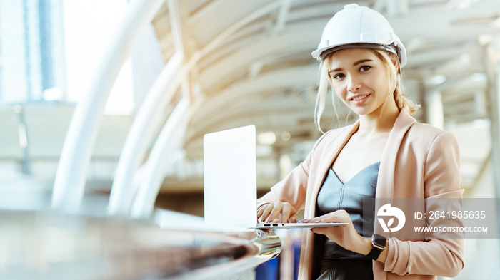 Businesswoman wearing helmet, white construction worker standing, using  laptop to work On job site.