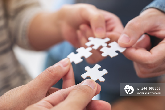 Closeup image of peoples hands holding and putting a piece of white jigsaw puzzle together