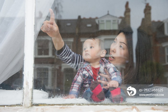 Mother and baby boy looking out of window, view through window