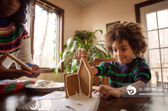 Boy (6-7) making gingerbread house with woman