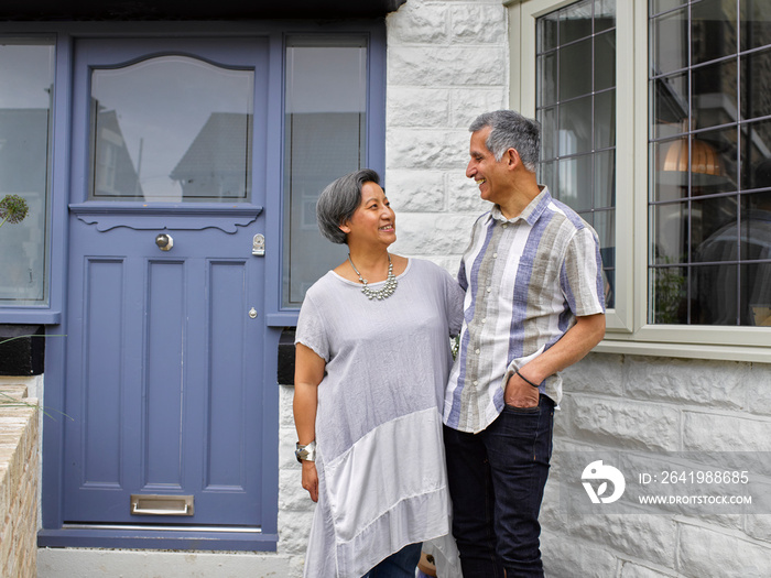 Smiling couple standing in front of house