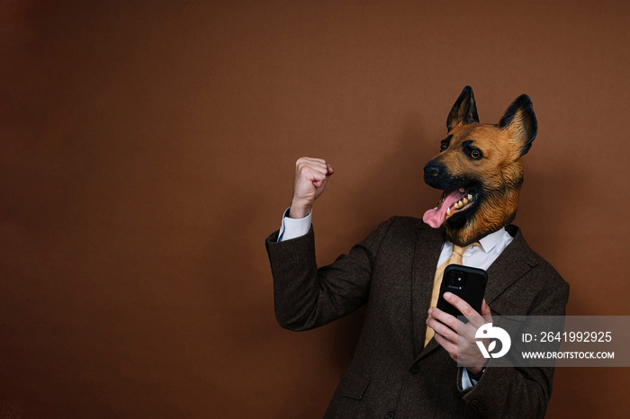 An elated man with smartphone and a latex dog head mask raising his hands