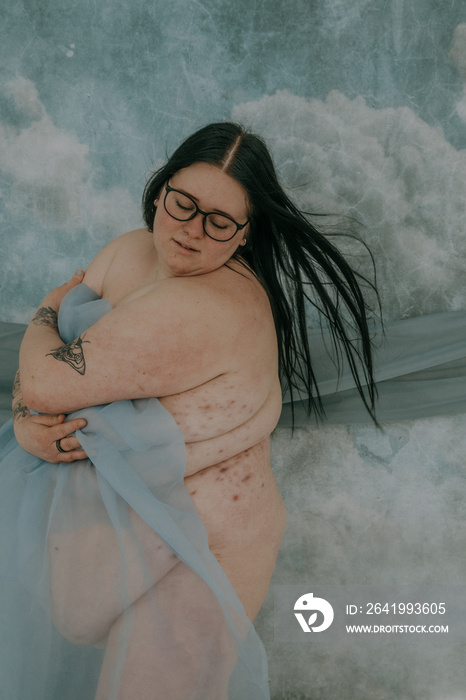 fat woman with hidradenitis suppurativa wearing glasses and holding blue fabric to body