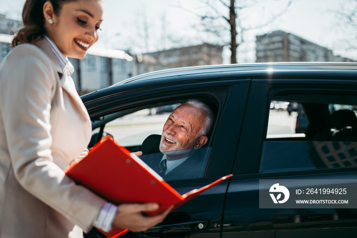 Beautiful young woman sales manager showing car specification to happy senior man buyer.