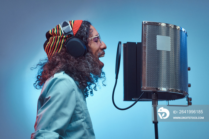 African Rastafarian singer male wearing a blue shirt and beanie emotionally writing song in the reco