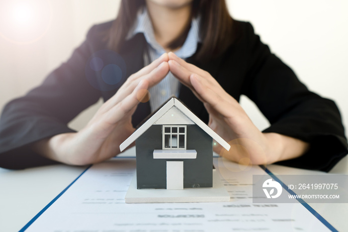 The hand of a home insurance broker protecting the small home on the desk.