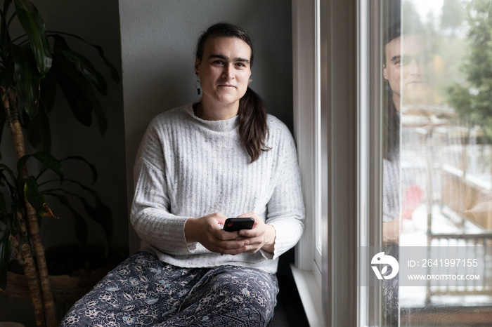 Non-binary person uses phone by the windowsill.