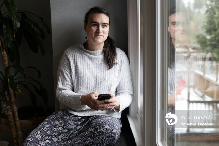 Non-binary person uses phone by the windowsill.