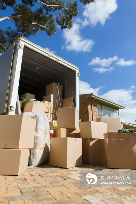 Cardboard boxes and moving van in sunny driveway outside house