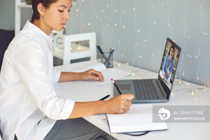 Young woman taking notes during online consultation with coach or video lesson with teacher