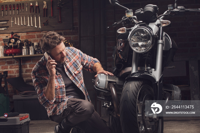 Man talking by the phone kneeling at motorcycle