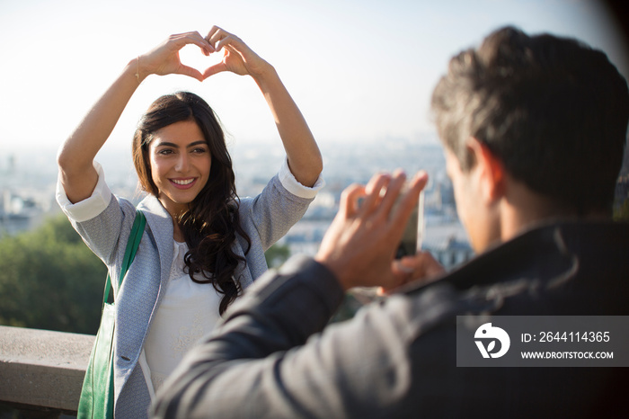 Woman posing with heart-shape hands for boyfriend on sunny balcony