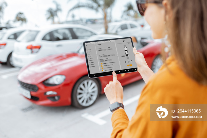 Woman controlling car with mobile application while standing near the vehicle outdoors, close-up vie