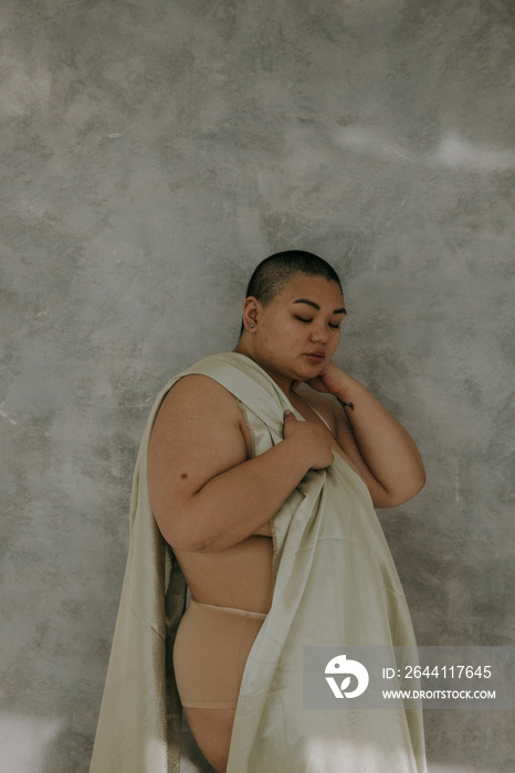 far away portrait of a plus size filipino woman with a shaved head eyes closed on a textured backdro