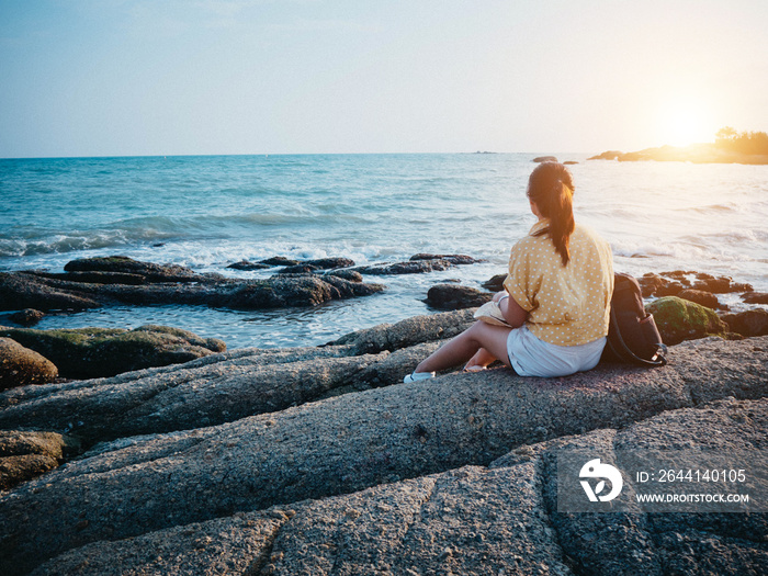 Woman looking to the sea and sitting on the rock. Hipster woman travel at the beach.