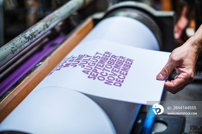 Mans hand taking printed sheet out of roller in workshop