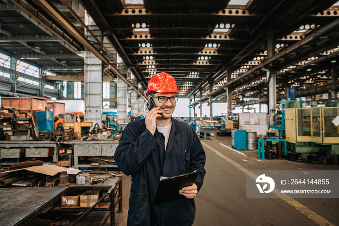 Worker talking on mobile phone at metal manufacturing plant.