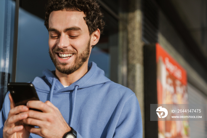 Happy handsome guy smiling and using mobile phone