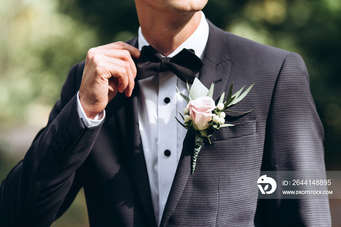 the groom in a suit straightens his tie bubochku. boutonniere on the lapel of his jacket. young man 