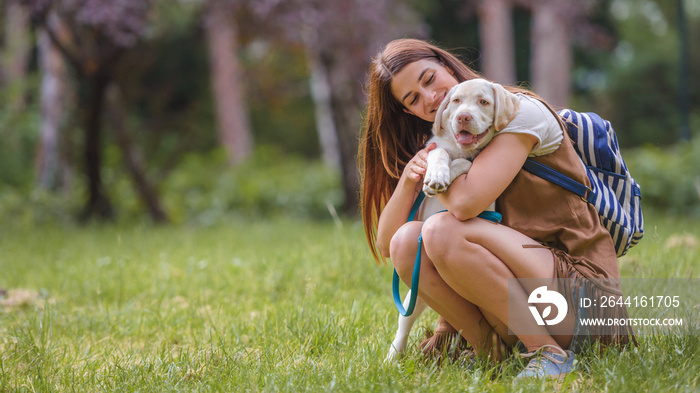 Beautiful young woman playing with a puppy labrador in the park