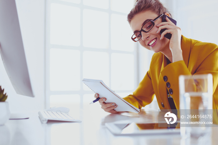 Portrait of beautiful woman making call while sitting at her workplace in front of laptop and workin