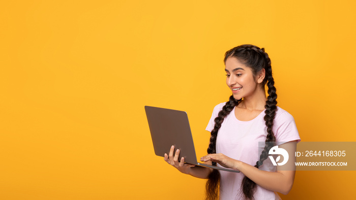 Smiling young indian lady holding and using laptop at studio