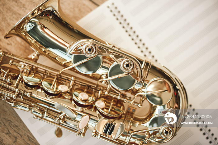 The joy of sax. Top view of beautiful shiny saxophone lying on sheets for music notes over wooden fl