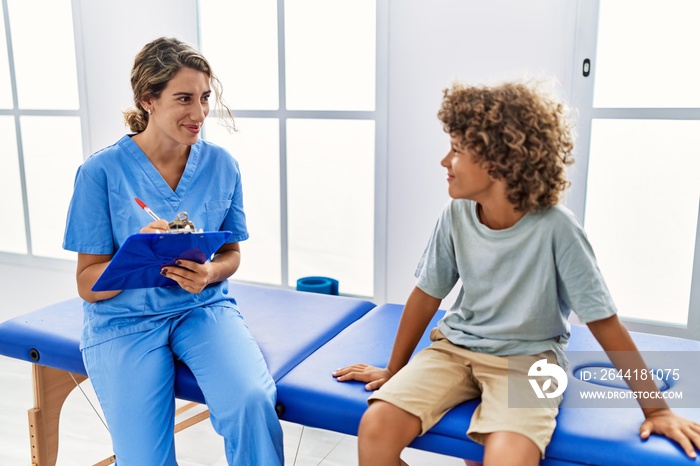 Mother and son wearing physiotherapist uniform having rehab session writing on clipboard at physioth