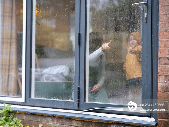 Mother and daughter looking through window during rain�