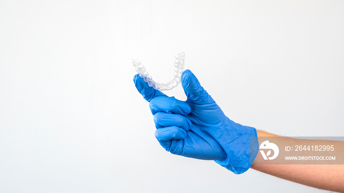 Male hand in gloves holding dental aligner retainer on white background dentist