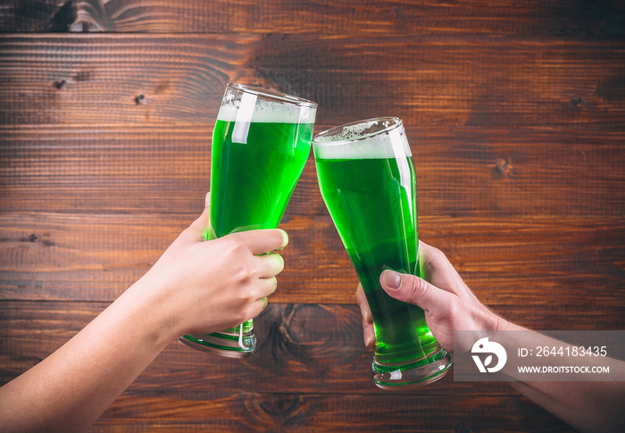 St Patricks Day concept two mug on hands green beer against wooden background