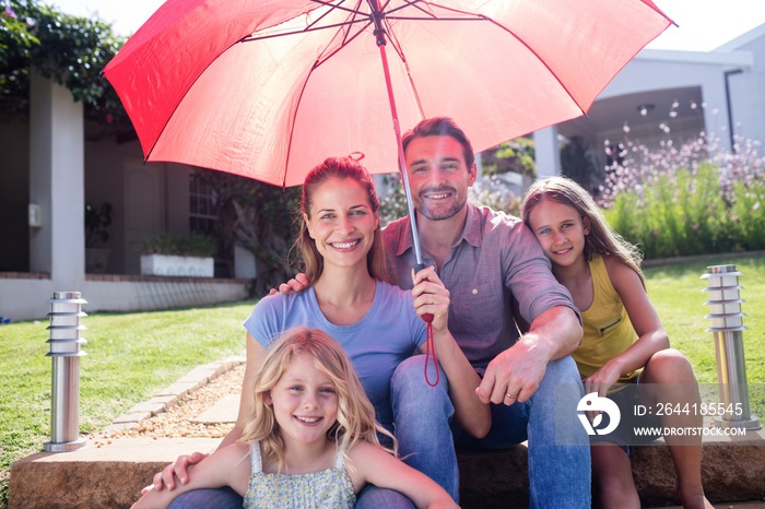 Happy family sitting in garden under a red umbrella