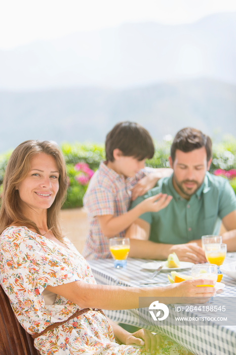 Portrait happy woman enjoying breakfast with family on sunny patio