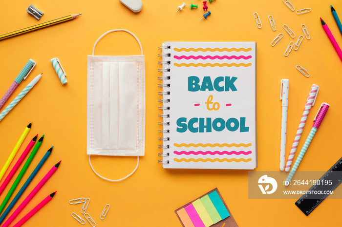 Stock photo of back to school in the new normal with a mask, a notebook with lettering and some stat