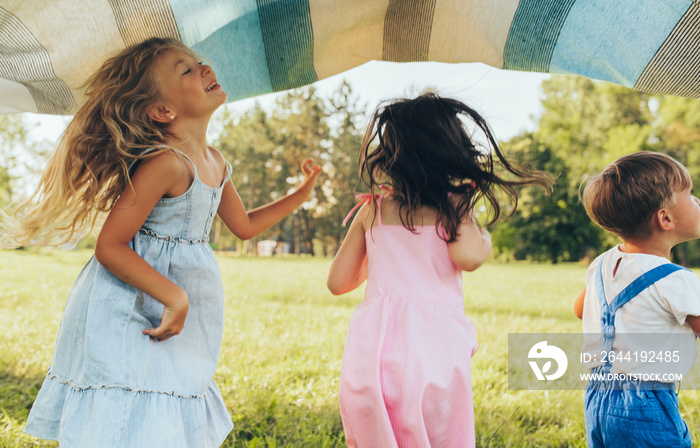 Playful children playing under the blanket, jumping and dancing together. Happy little boy and littl