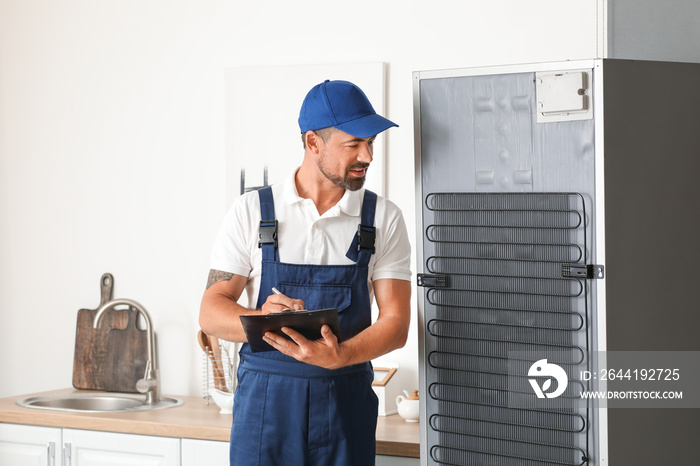 Worker of repair service near fridge in kitchen