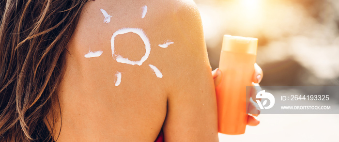 Woman wearing two piece bikini applying suncream with sun drawn on back and holding sunscreen lotion