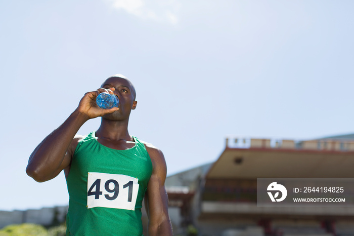 Male track and field athlete drinking sports drink on sunny field