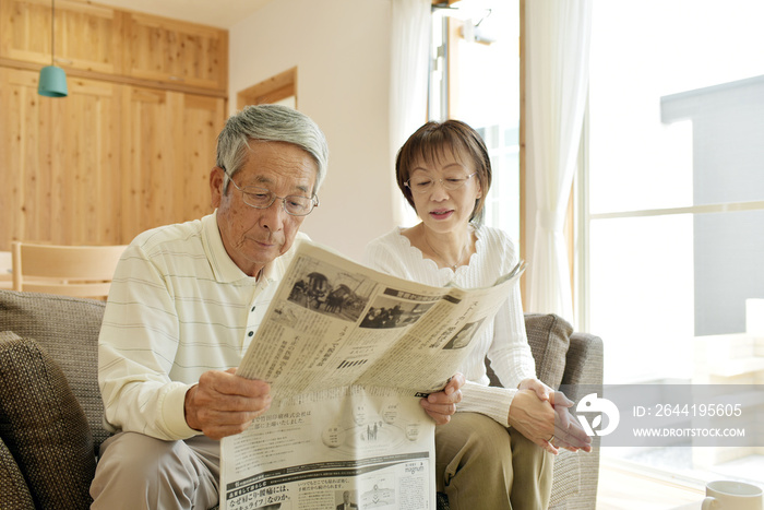 リビングのソファで新聞を読むシニア夫婦