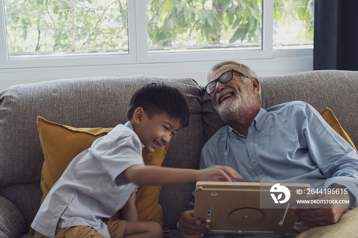 senior man happiness and grandson are sitting on the sofa and playing games and reading book at livi