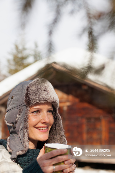 Smiling woman drinking hot cocoa outside cabin