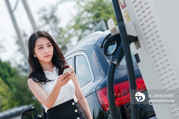 青年女人使用手机自助充电汽车