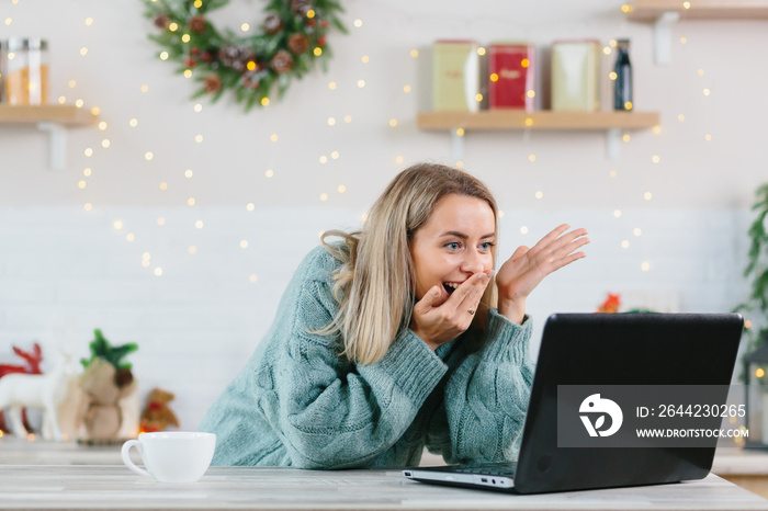 A woman shocked with happiness rejoiced looking at a laptop monitor at home during the New Year and 