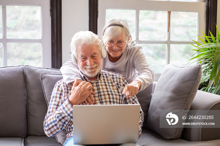 Happy 70s white-haired couple sitting on couch, wife showing wished product in internet store on dig