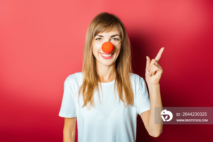 Young beautiful woman with a red nose of a clown on a pink background. Concept red nose day, holiday