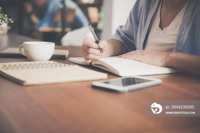 Young business woman in white dress sitting at table in cafe and writing in notebook. Asian woman ta