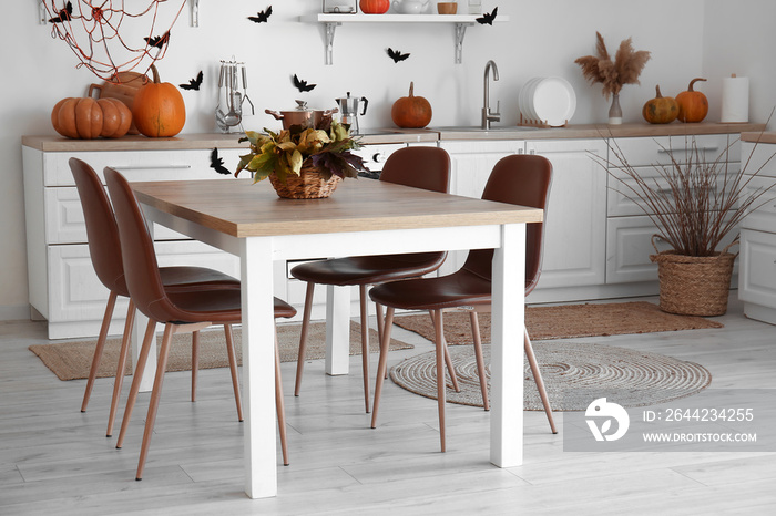 Interior of modern kitchen decorated for Halloween with pumpkins, dining table and counters