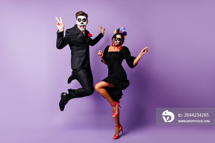 Full-length portrait of european couple dancing on purple background in zombie costumes. Funny young